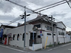 Urban street corner with tangled overhead power lines above a white tiled building and storefronts.