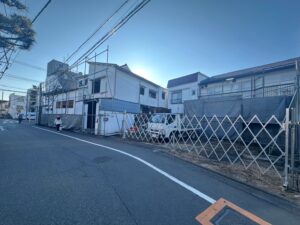 Residential street with a building under construction, metal scaffolding along the facade and a white van parked behind a crisscross fence.