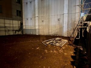 Construction site interior with dirt floor, metal wall panels, and scattered scaffolding on the right side.