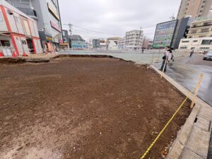 Urban construction site with a large dirt excavation area along a city sidewalk, cordoned off by yellow tape.