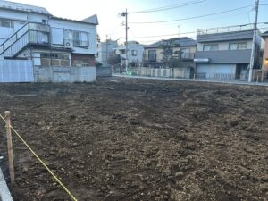 Wide view of a dirt lot in a residential area, with yellow caution tape and utility poles in the background.